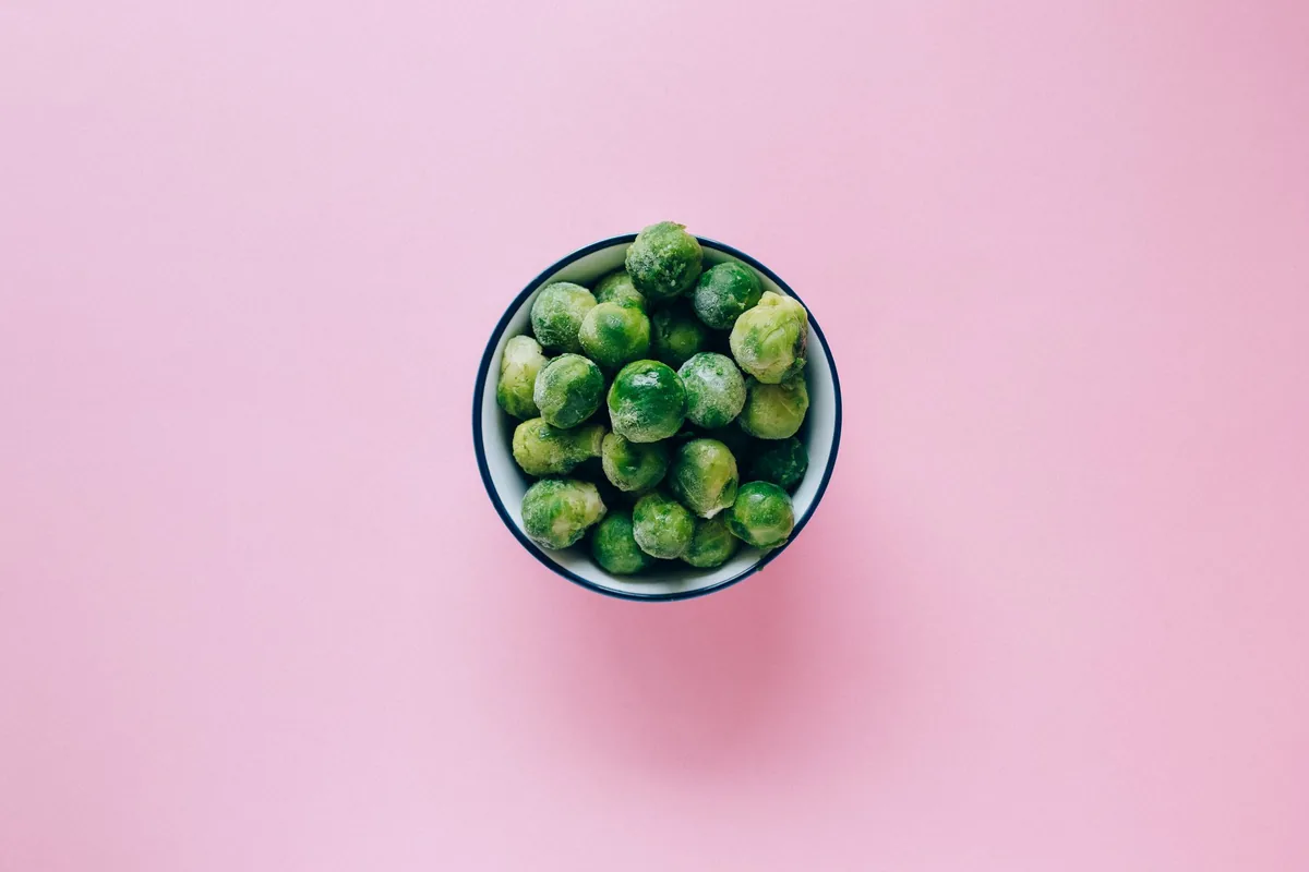 A bowl of frozen peas on a pink surface