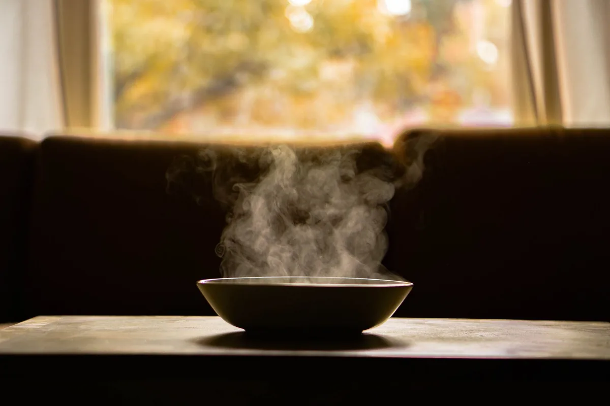 A bowl of hot soup with steam rising, on a wooden kitchen table