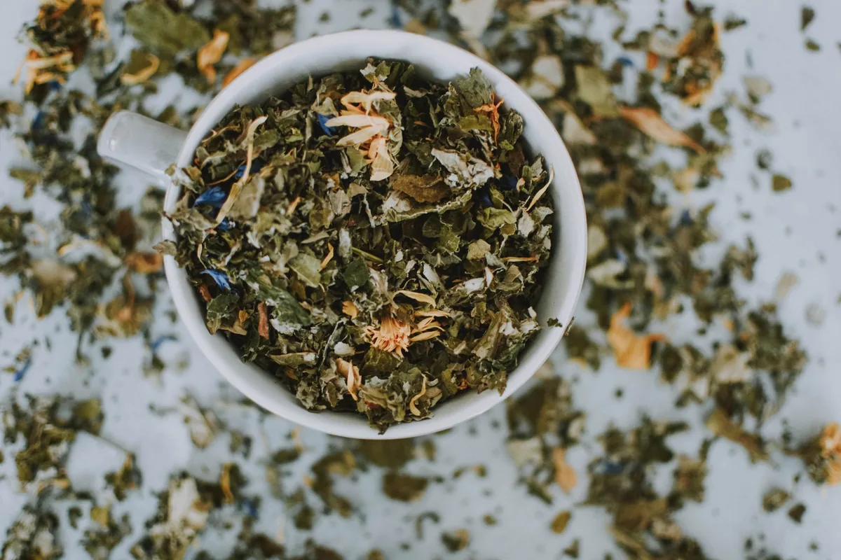 A bowl of loose dried tea leaves on a scattered bed of tea