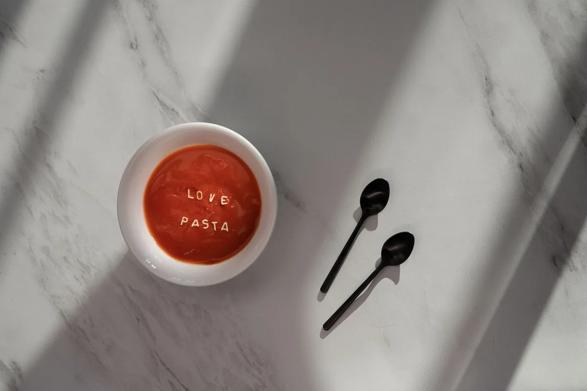 A bowl of tomato soup with pasta letters on a marble surface