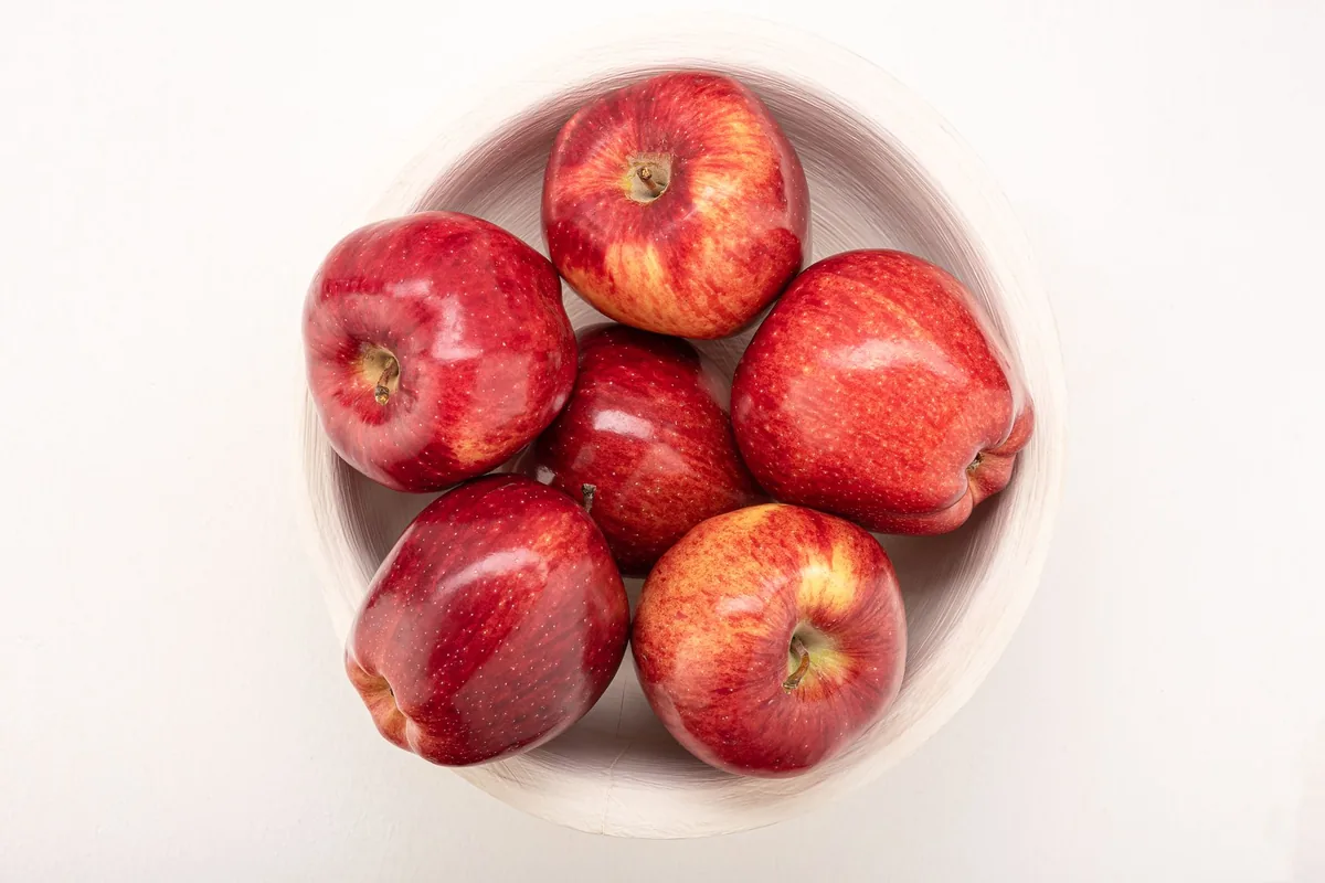 A bowl of whole red apples on a light wooden table