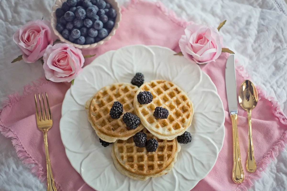 A breakfast table with a plate of waffles topped with mixed berries in daylight
