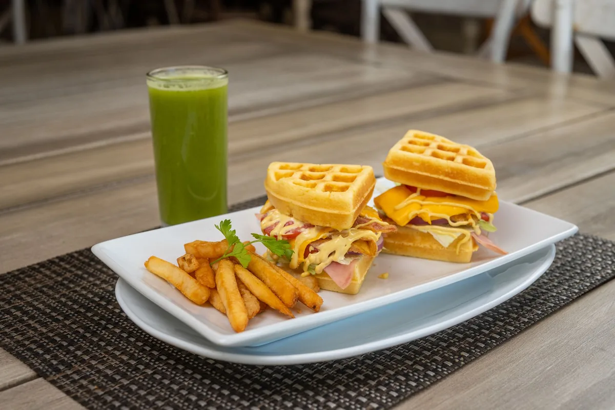 Waffle sandwiches with fries and a green juice on a table