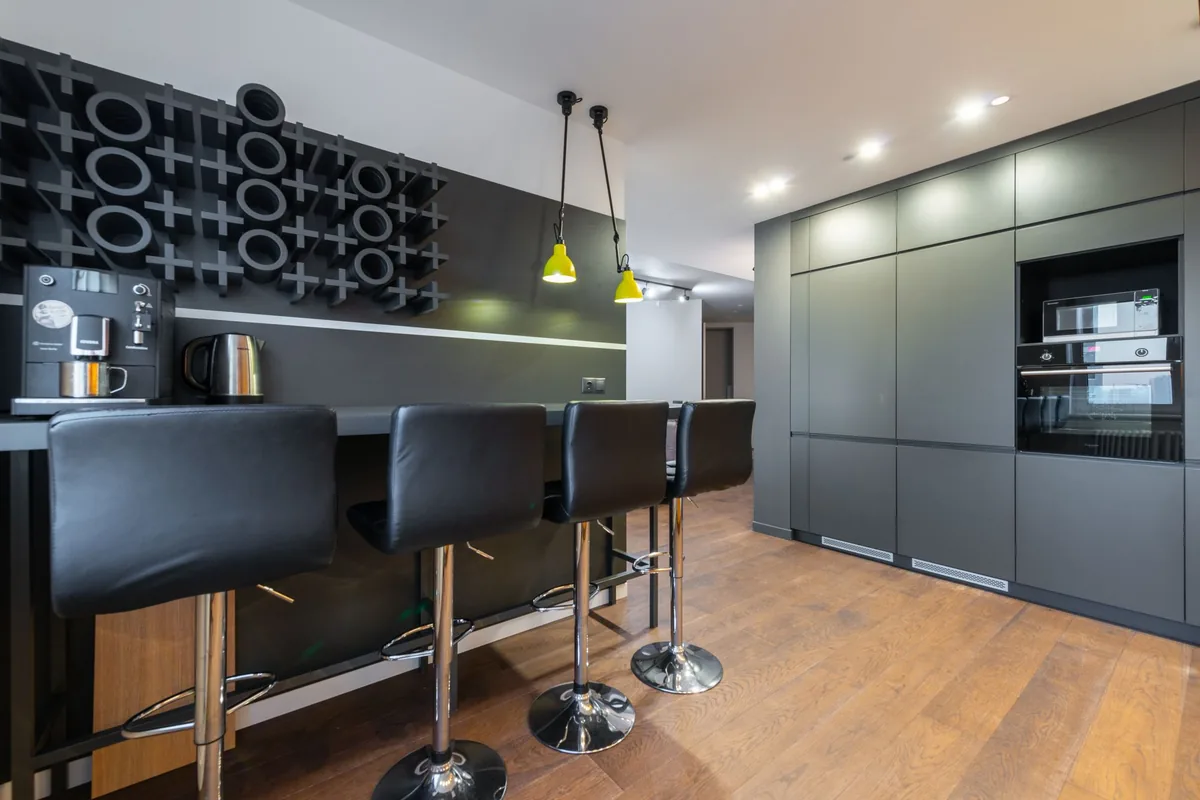 A modern dark kitchen with bar stools and a coffee machine