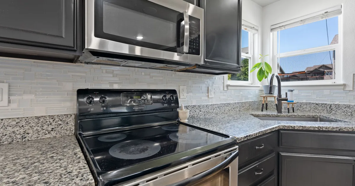 A bright kitchen with a stainless steel microwave mounted above a range between white cabinets