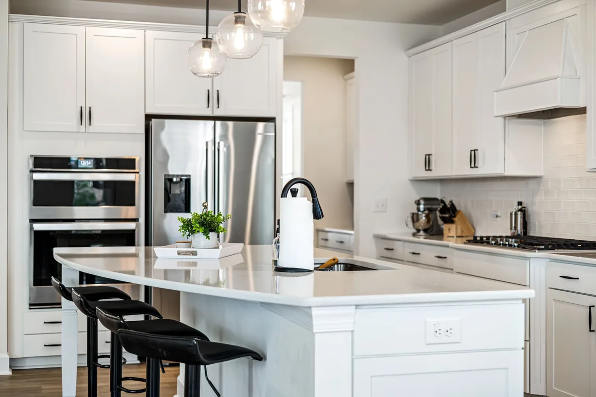 A white kitchen with an island, wall ovens and a cabinet-style hood