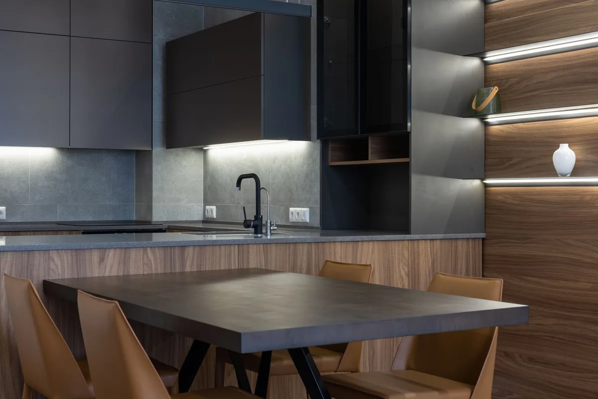 A dark modern kitchen with a dining table and wall cabinets
