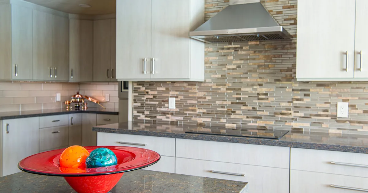A kitchen with a stainless chimney hood over a mosaic tile backsplash
