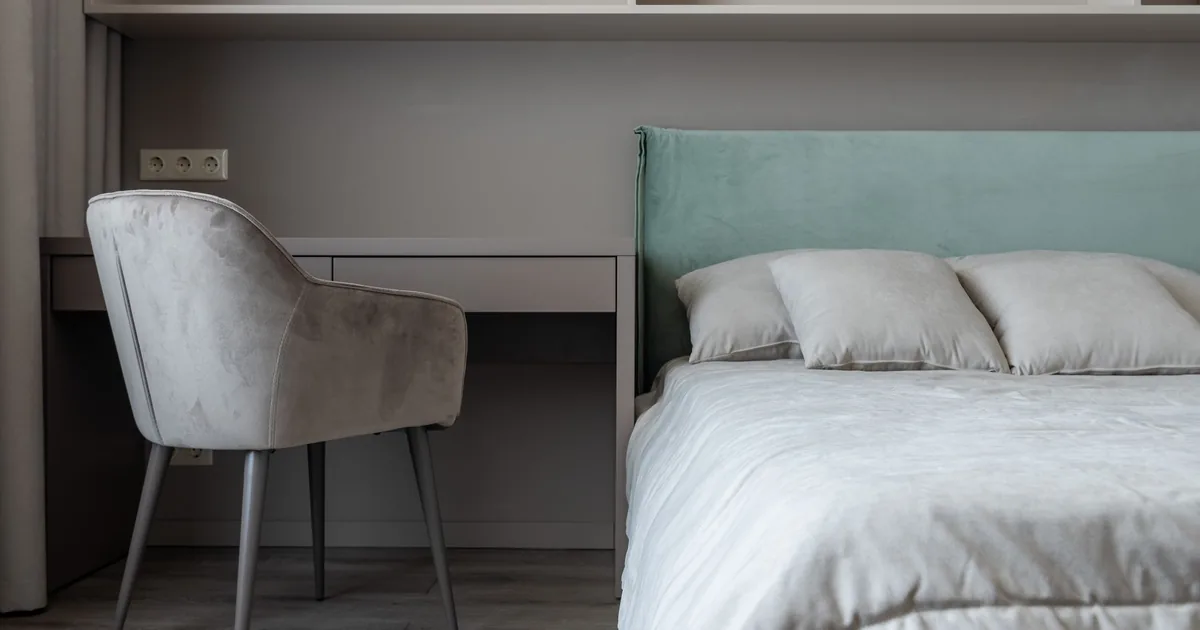 A bright, tidy bedroom with a made bed, a small desk and a window letting in daylight
