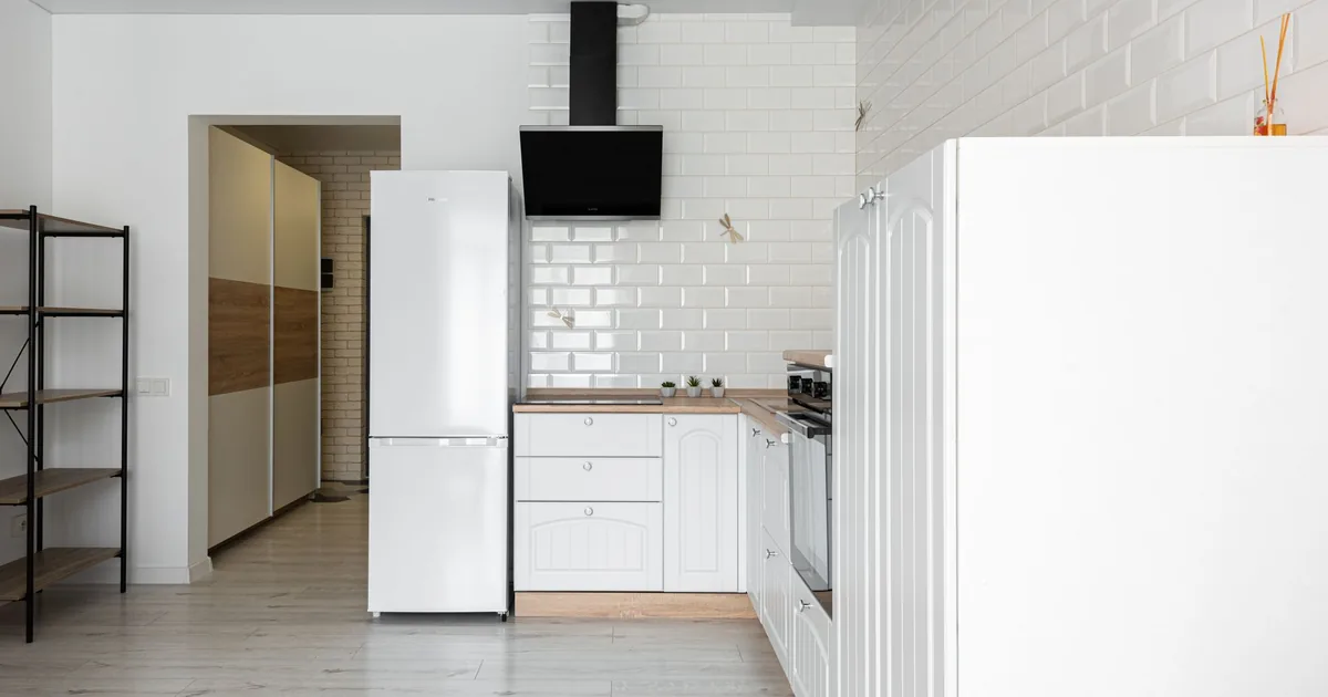 A bright white kitchen with a tall refrigerator beside the cabinets