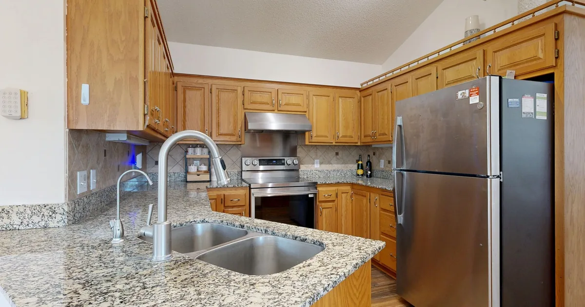 A brushed stainless steel double bowl sink set into a light stone countertop with a chrome faucet behind it