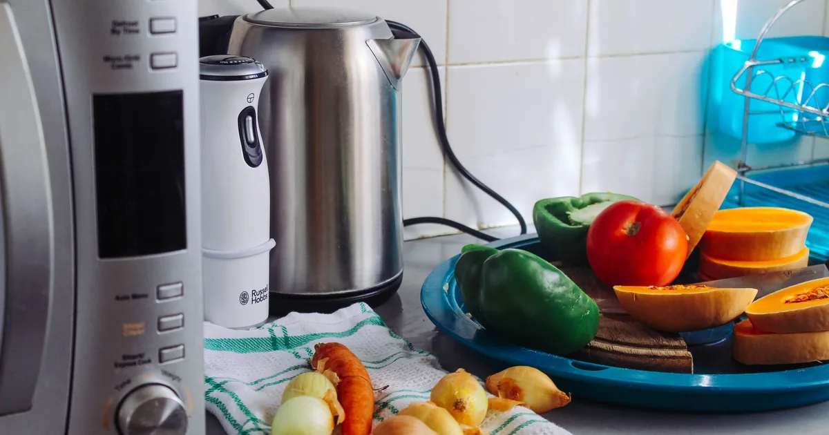 A stainless electric kettle beside a bowl of vegetables