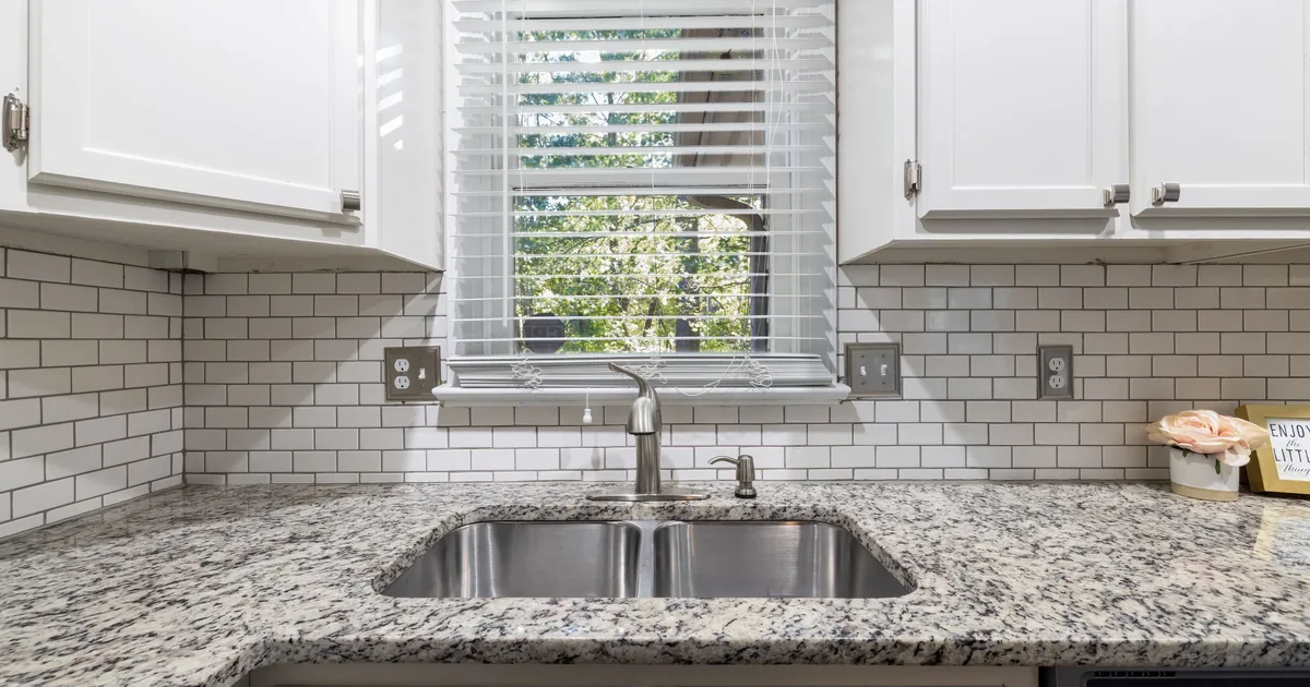 A brushed stainless steel single bowl sink set into a pale stone worktop in a bright kitchen