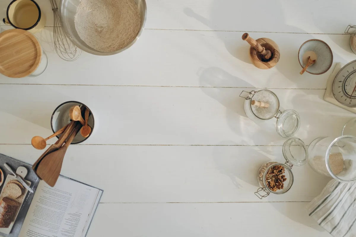 Wooden utensils in a crock among jars on a white table