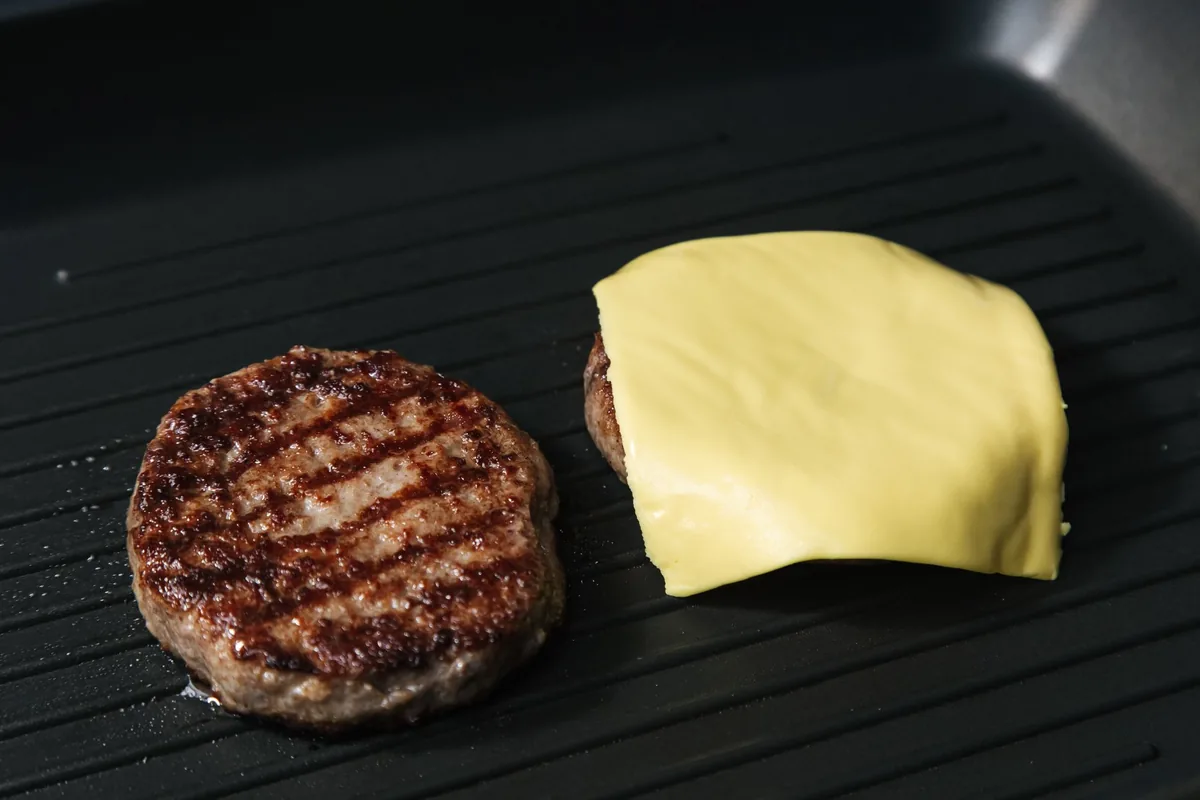 A burger patty and a cheese slice on a ridged nonstick grill plate