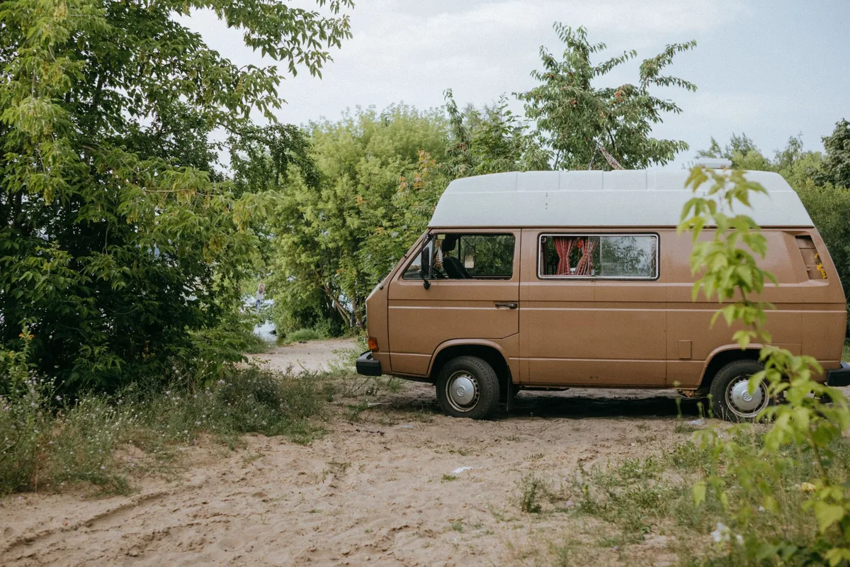 A camper van parked among trees beside a dirt track