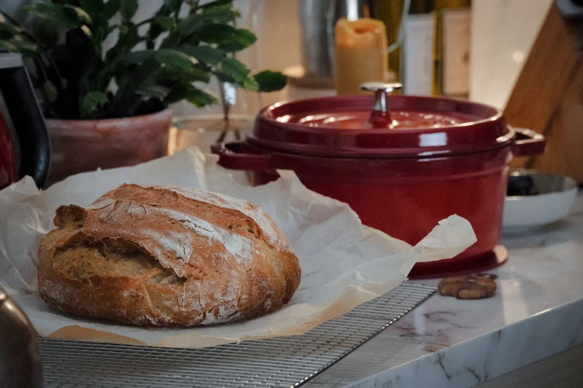 A cast-iron Dutch oven with a loaf of bread on a kitchen counter