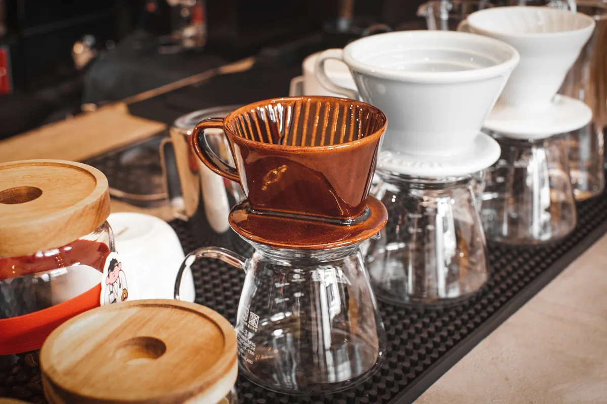 A ceramic pour-over dripper with a paper filter sitting on a glass carafe in bright daylight
