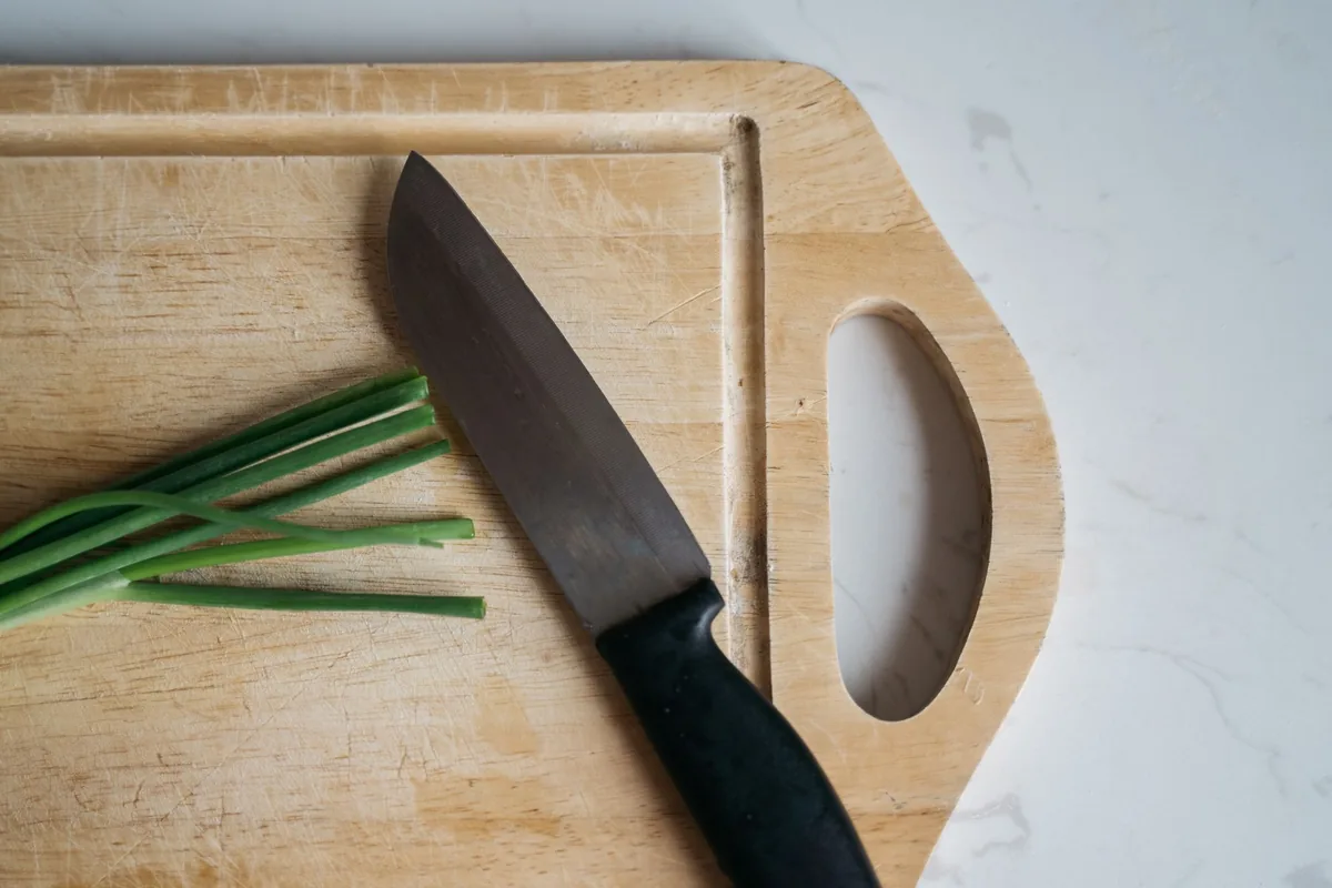 A chef knife and chives on a wooden cutting board
