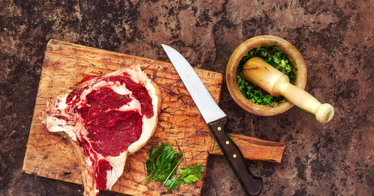 A chef knife beside a raw ribeye on a wooden board