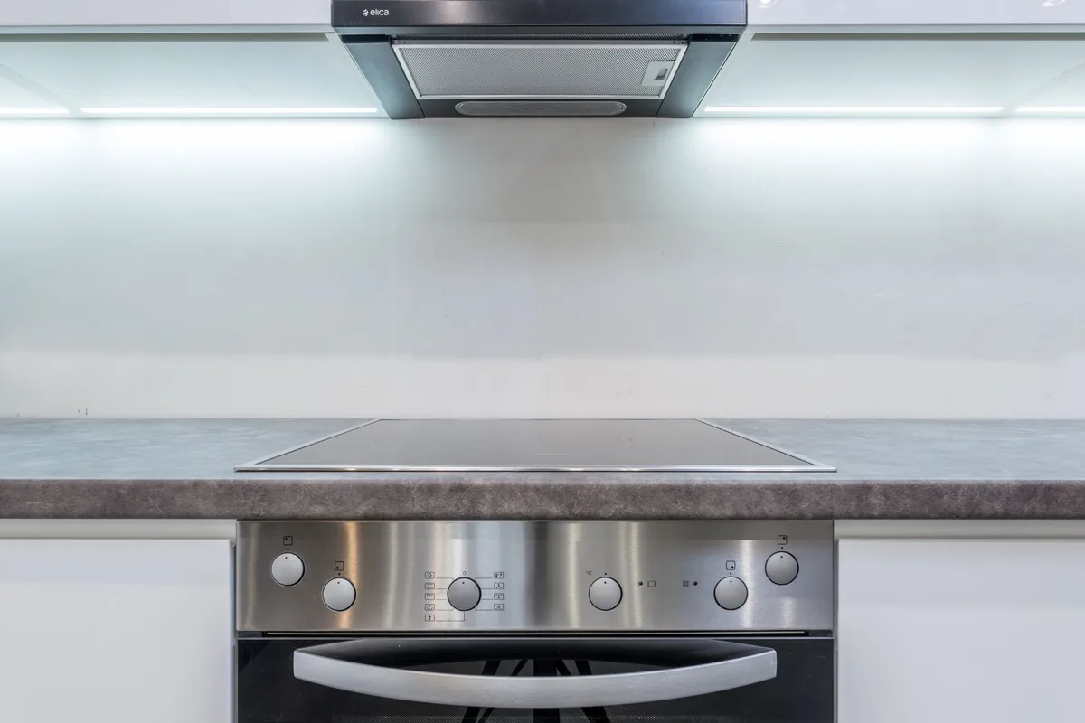 A clean white kitchen with a flush cooktop beneath an extractor hood