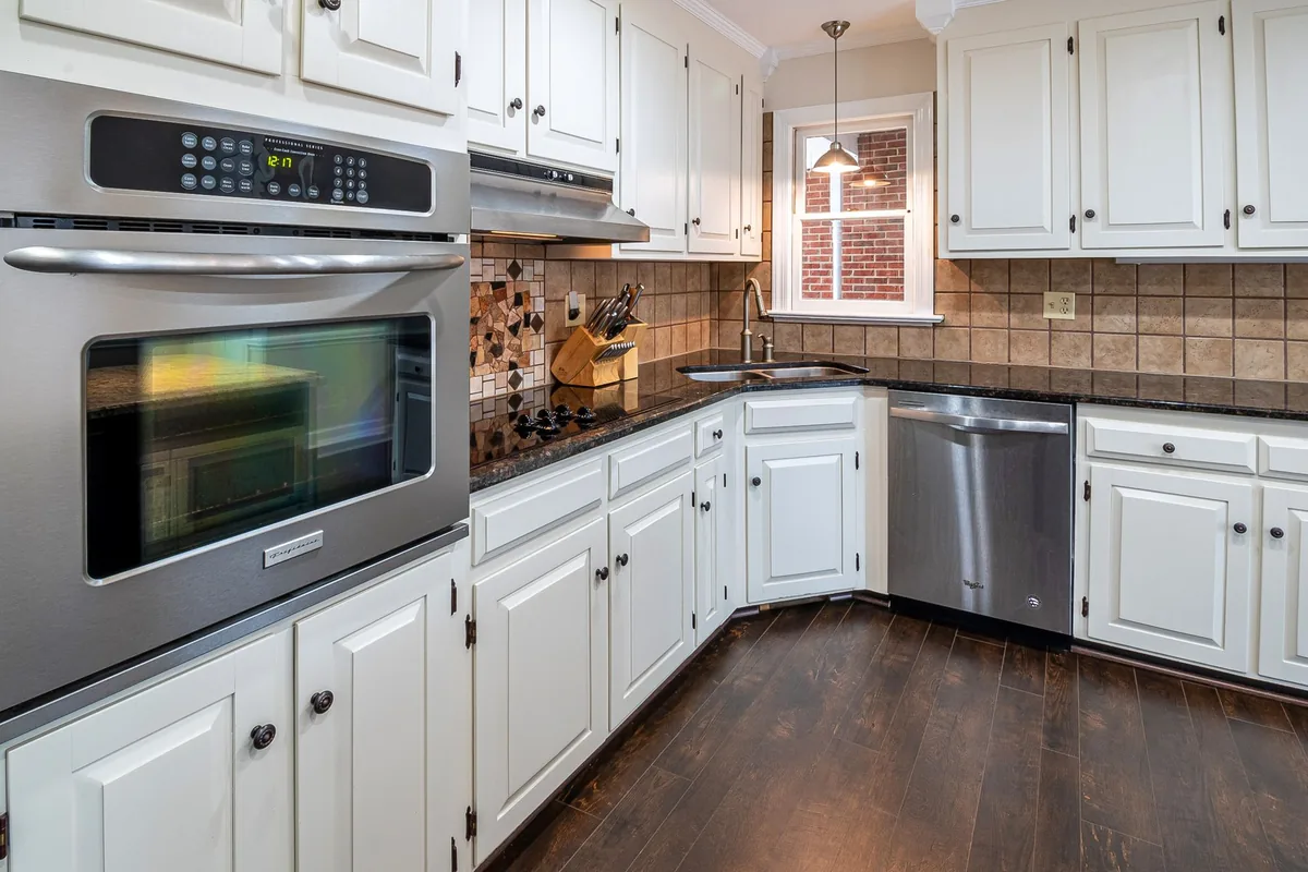 A white kitchen with a wall oven and a wooden floor