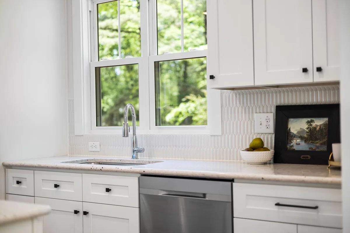 A clean white kitchen with a window over the sink