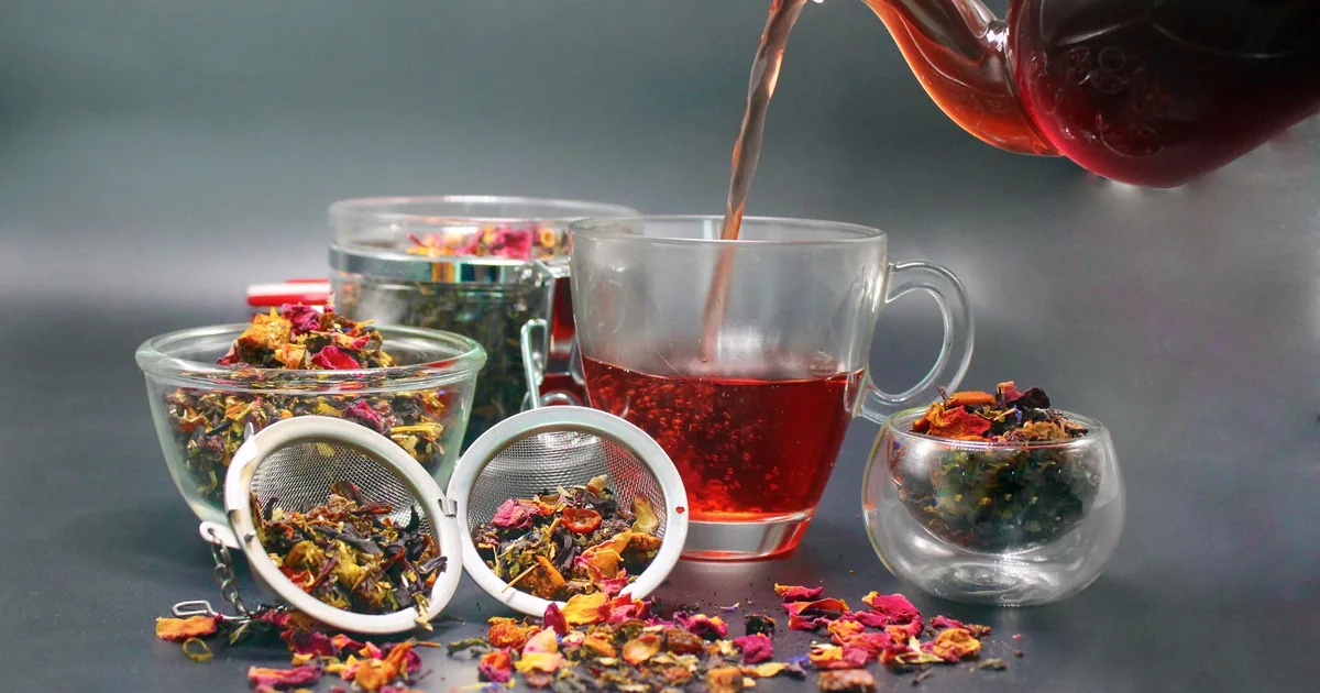 Tea pouring into a glass cup beside a tea ball and dried flowers