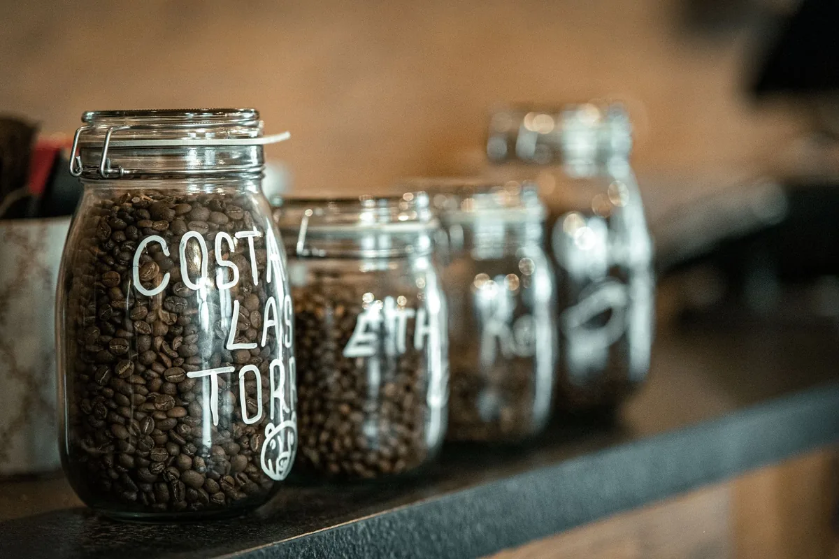 A clear glass jar filled with roasted coffee beans on a light kitchen counter