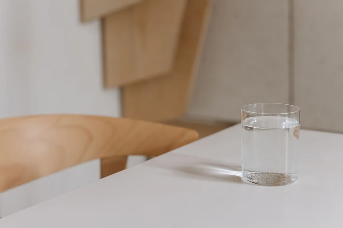 A clear glass of water standing on a light wooden table near a bright window