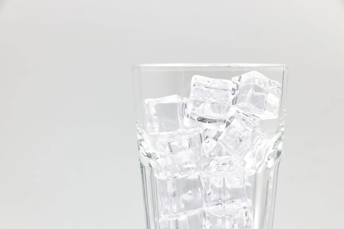 A clear glass packed with ice cubes and water on a light surface