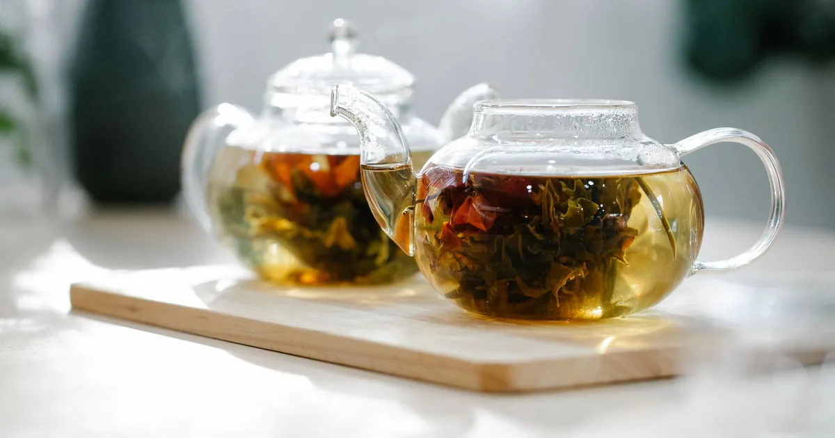 A clear glass teapot of brewed tea beside a small dish of loose tea leaves