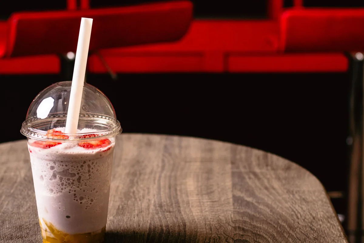 A clear plastic cup of berry smoothie with a domed lid and straw on a sunny table