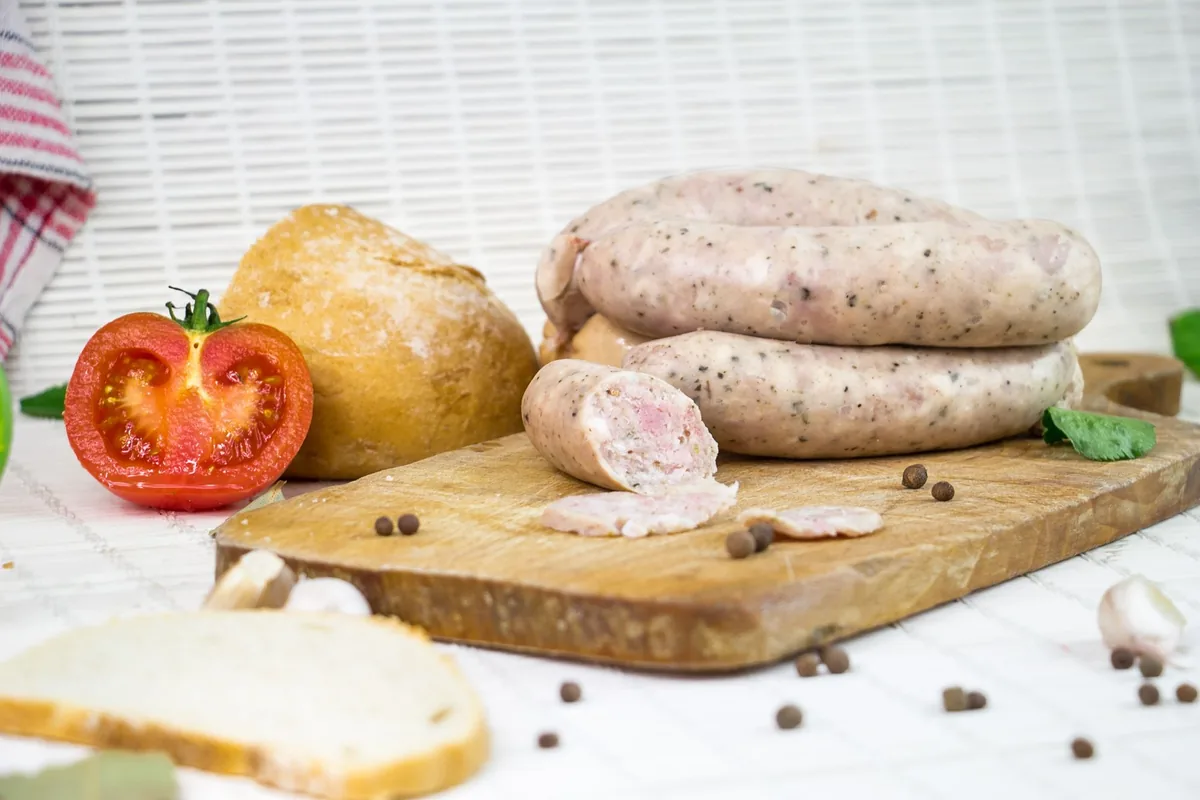 A coil of raw homemade sausages on a wooden board with herbs