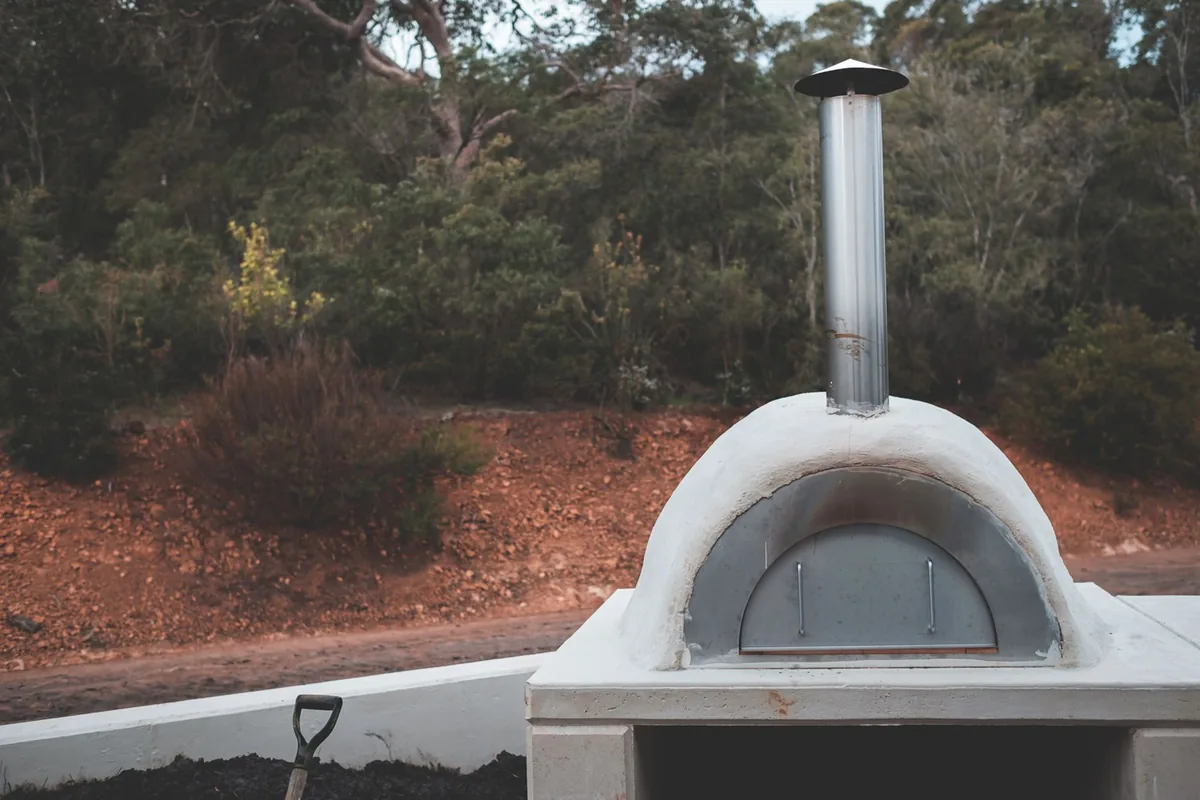 A white pizza oven with a chimney on a stand outdoors