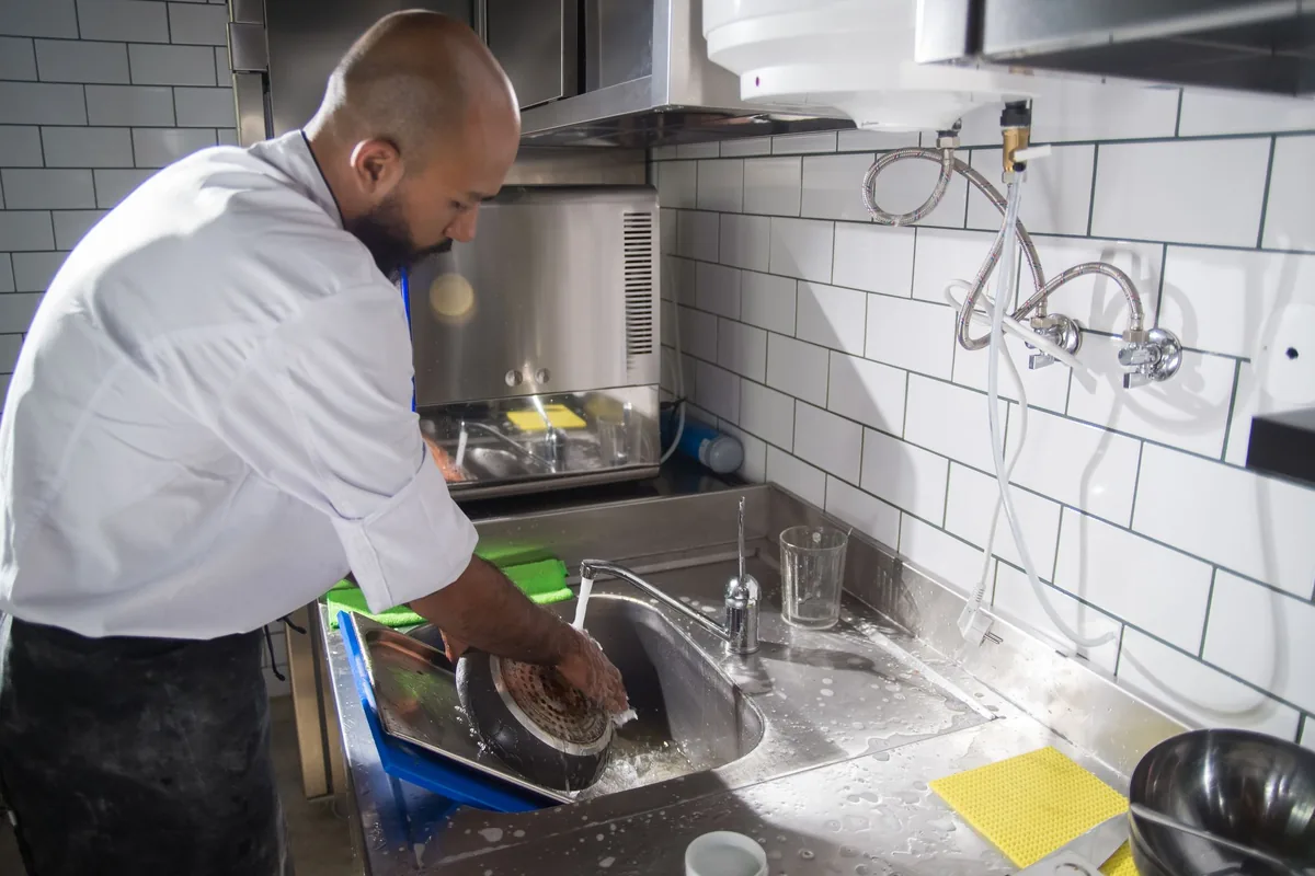 A cooking pot being washed by hand in a kitchen sink