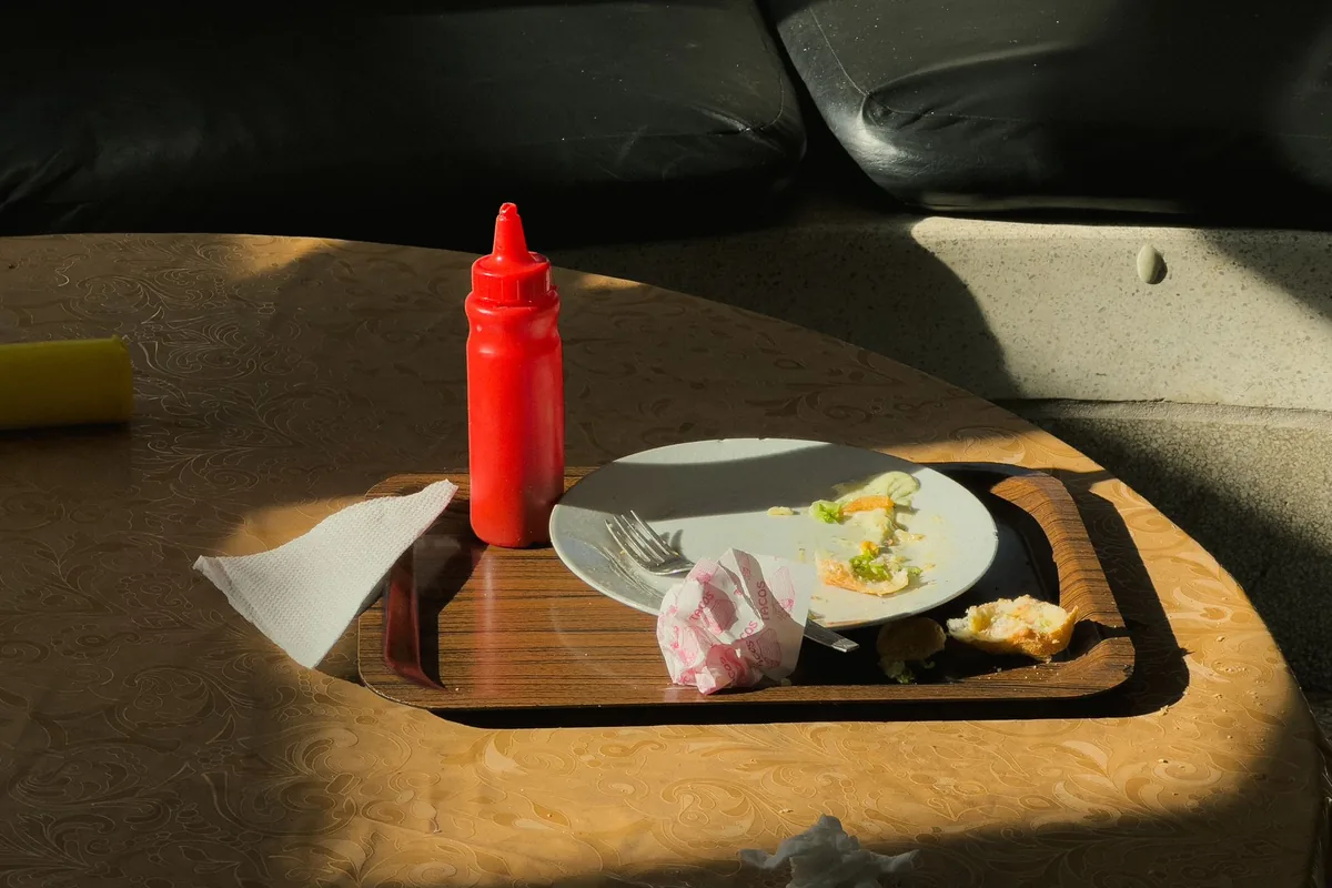 A tray with a plate of leftovers and a bottle of ketchup in afternoon light