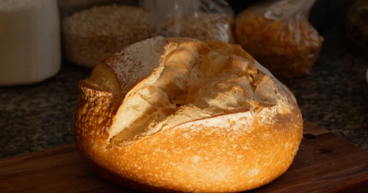 A crusty loaf of bread resting on a wooden kitchen counter in soft daylight