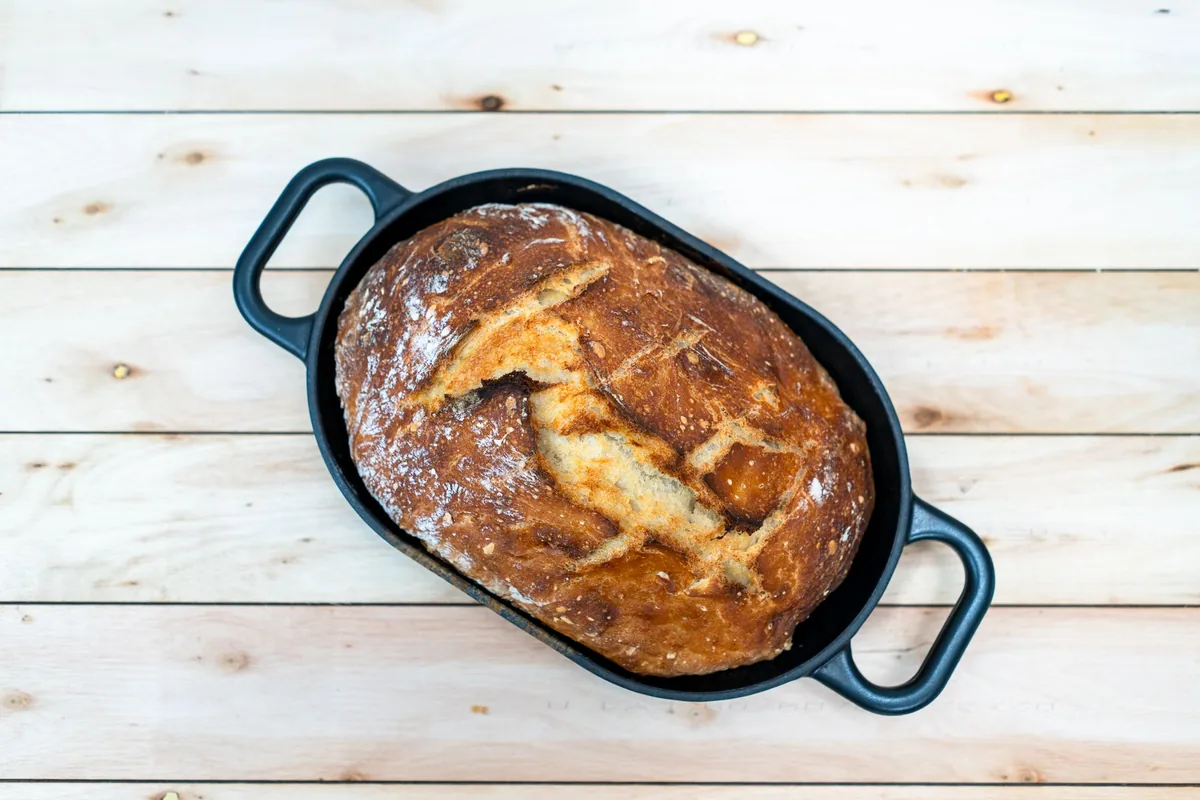 A crusty round loaf of bread in a lidless pot fresh from the oven