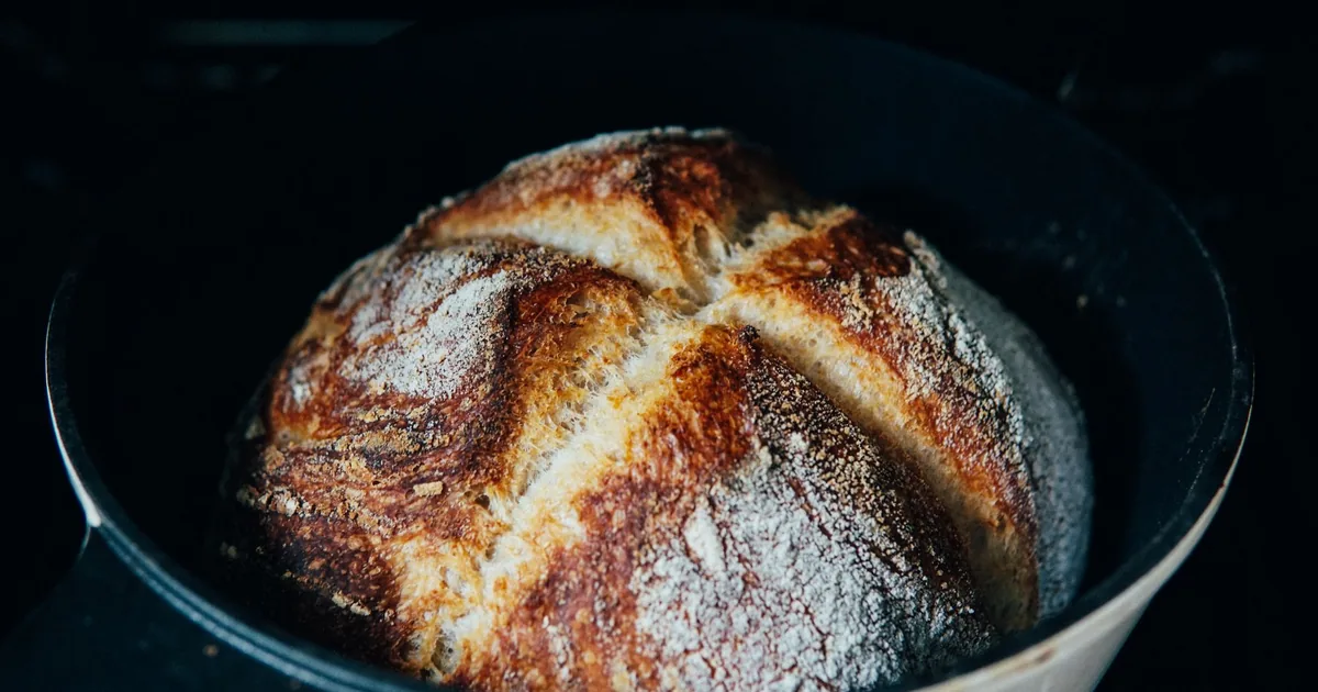 A crusty round sourdough loaf sitting in an open cast iron Dutch oven