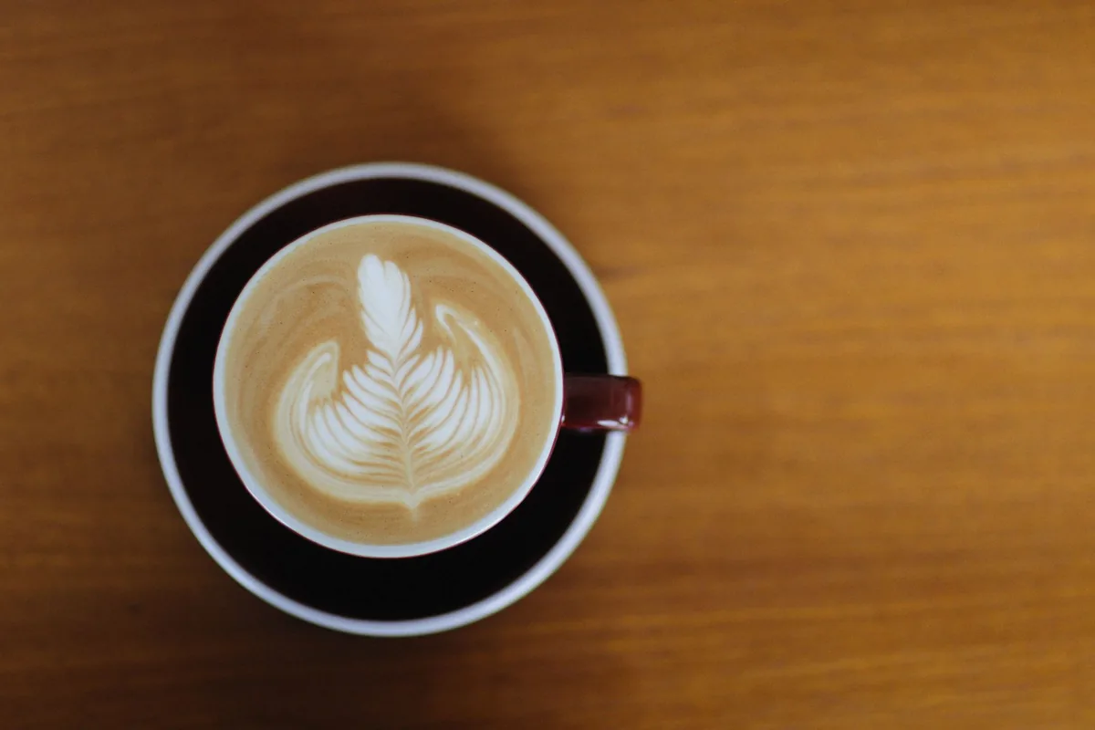 A cup of latte with a leaf pattern in the milk foam on a wooden table