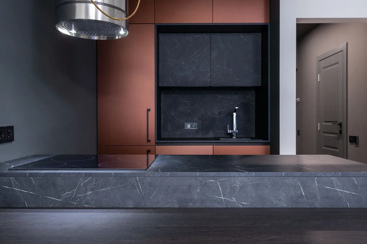 A dark modern kitchen with a stone island