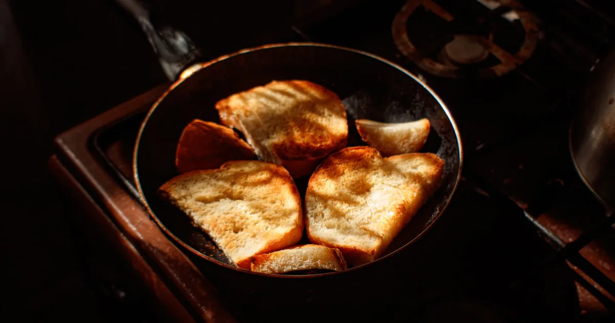 A dark nonstick frying pan sitting on a lit gas burner on a clean kitchen hob