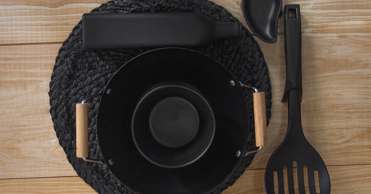 A dark pan with a wooden-handled spatula on a woven mat