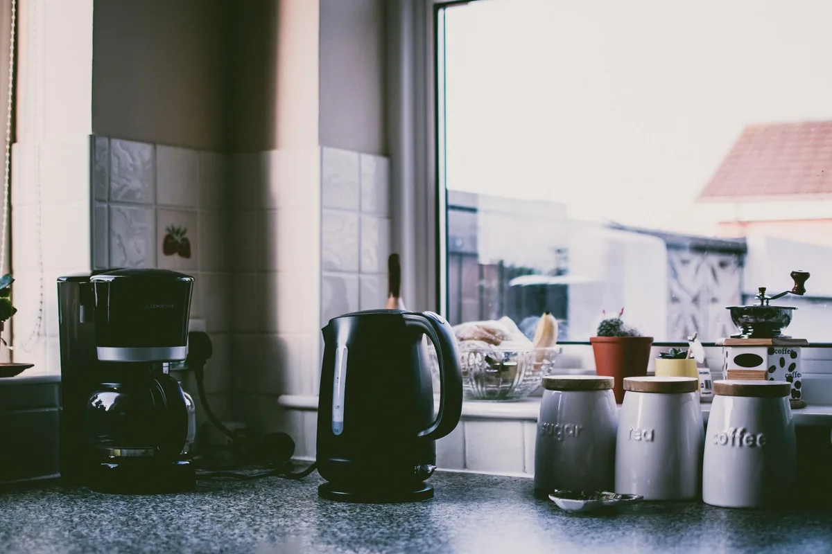 A drip coffee maker and a kettle on a kitchen worktop by a window