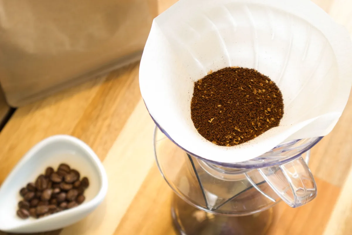 A filter basket filled with fresh ground coffee on a light surface