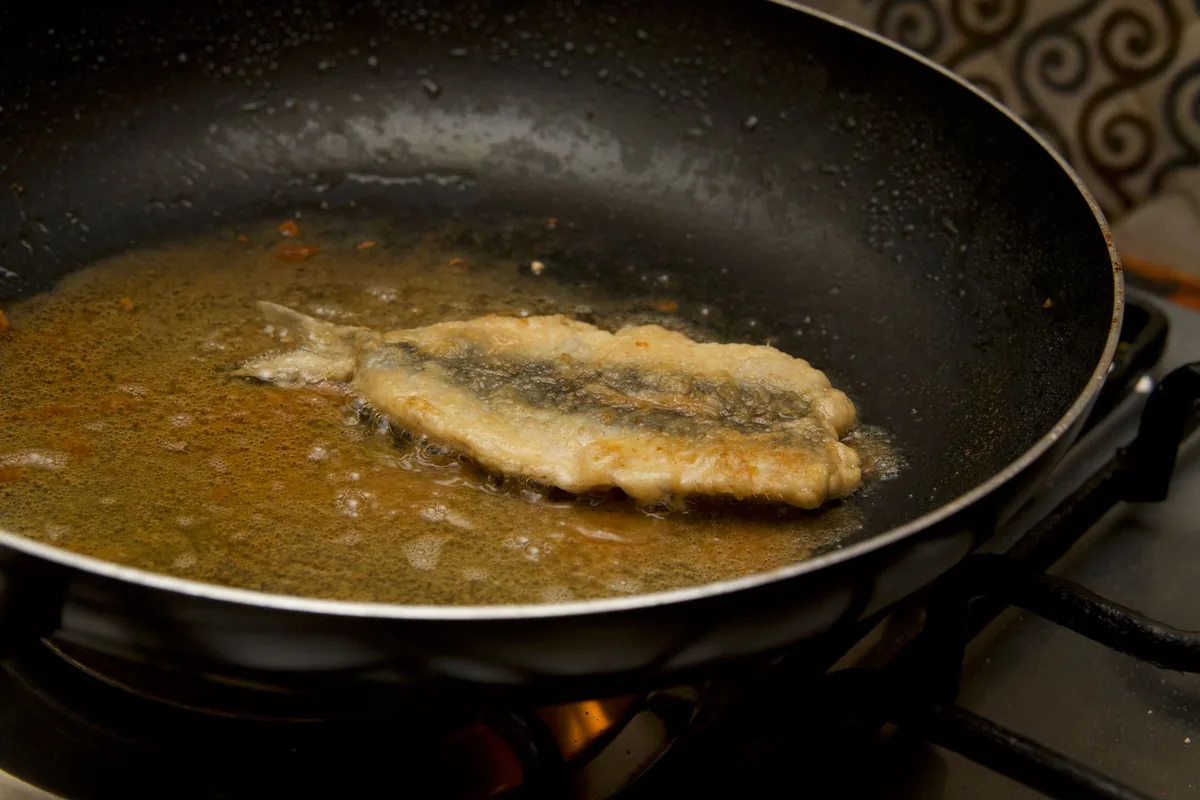 A fish fillet frying in a dark nonstick pan