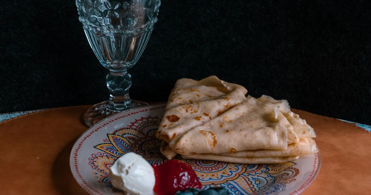 A folded thin crepe on a white plate topped with fresh berries and a dusting of sugar