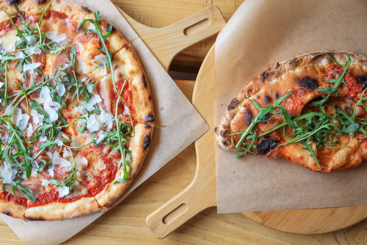 Two thin-crust pizzas with rocket on wooden peels