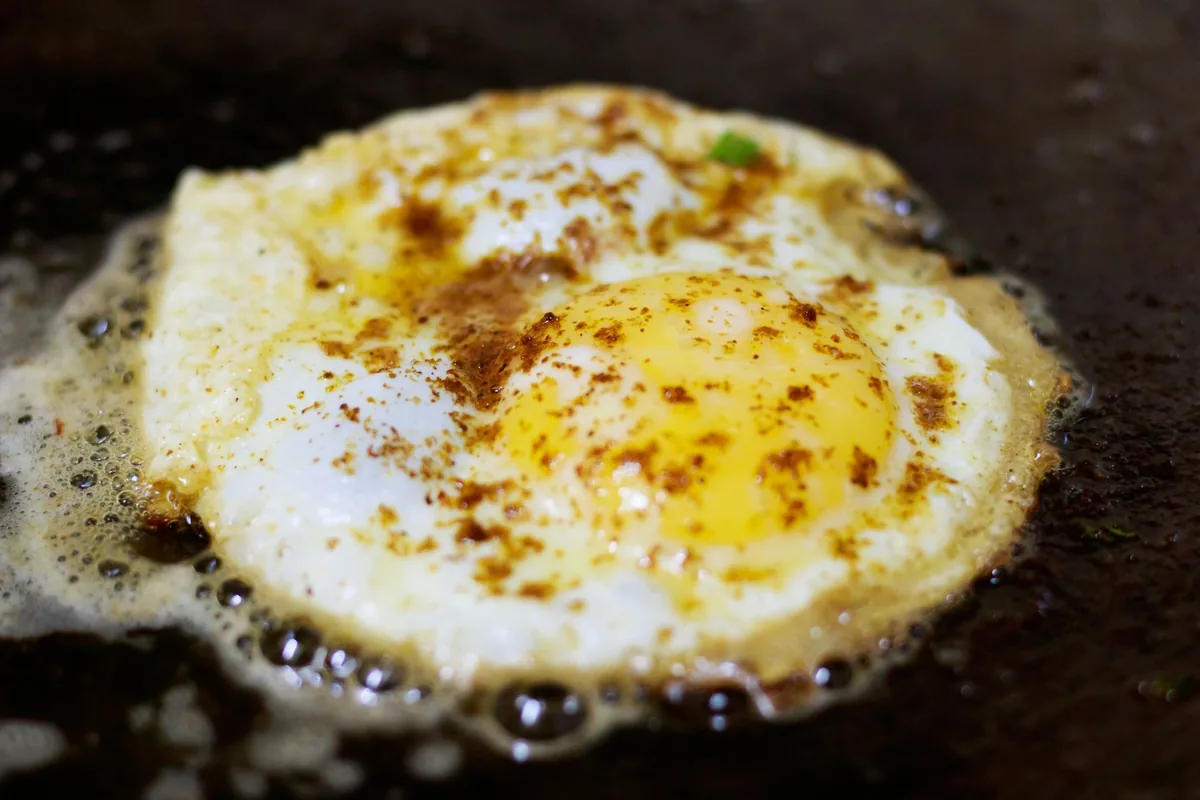 A fried egg sizzling in oil in a dark pan